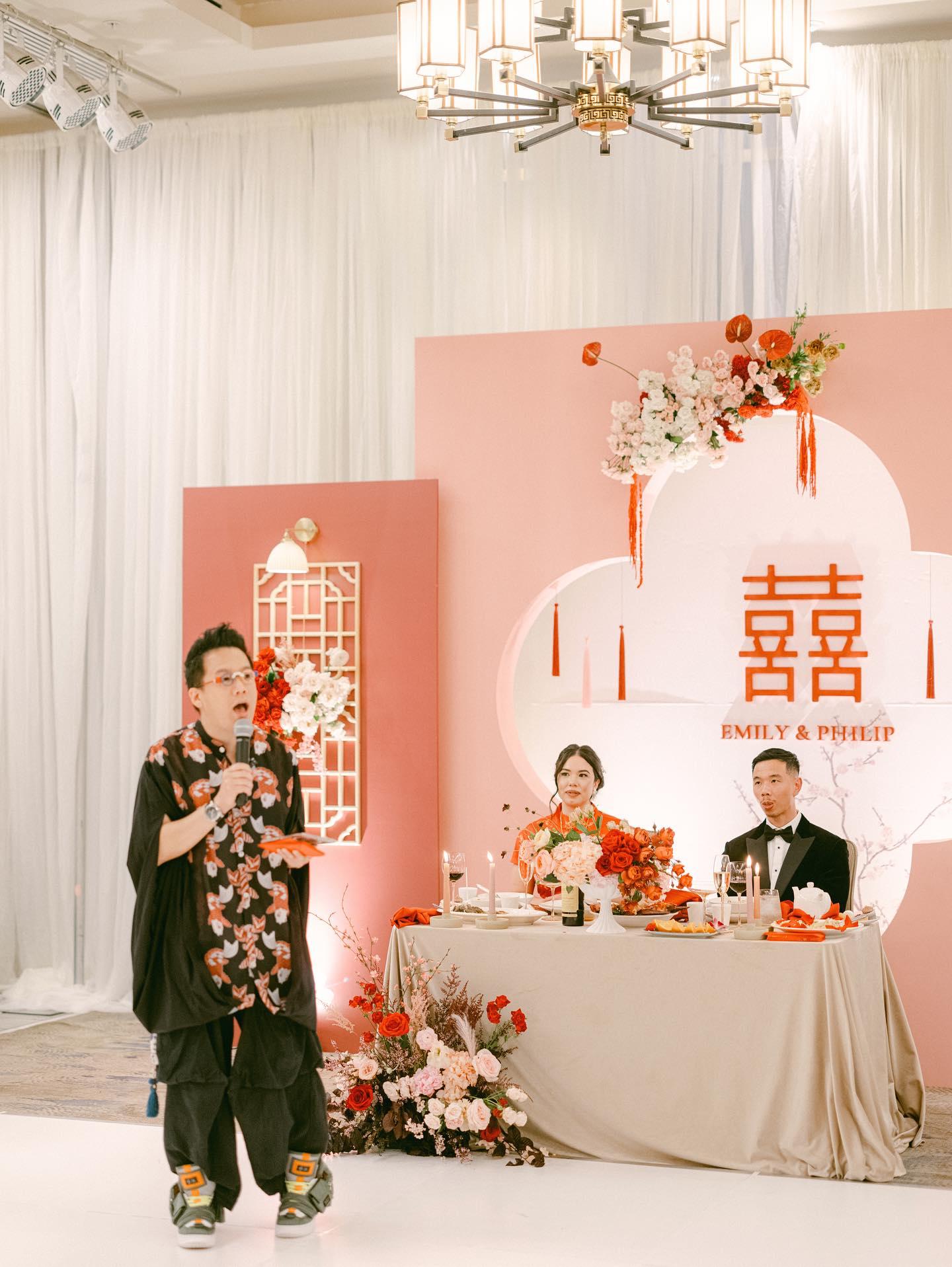 Foksifu emceeing a Chinese wedding reception with a double happiness backdrop and floral arrangements at a Bay Area banquet