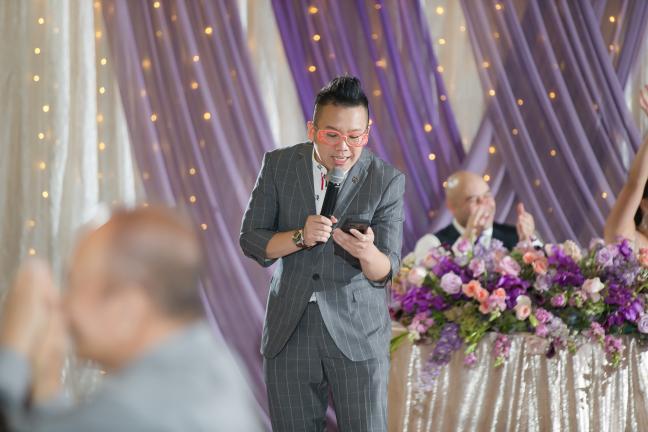 Foksifu on the microphone hosting a wedding reception with purple and white draping backdrop in the Bay Area