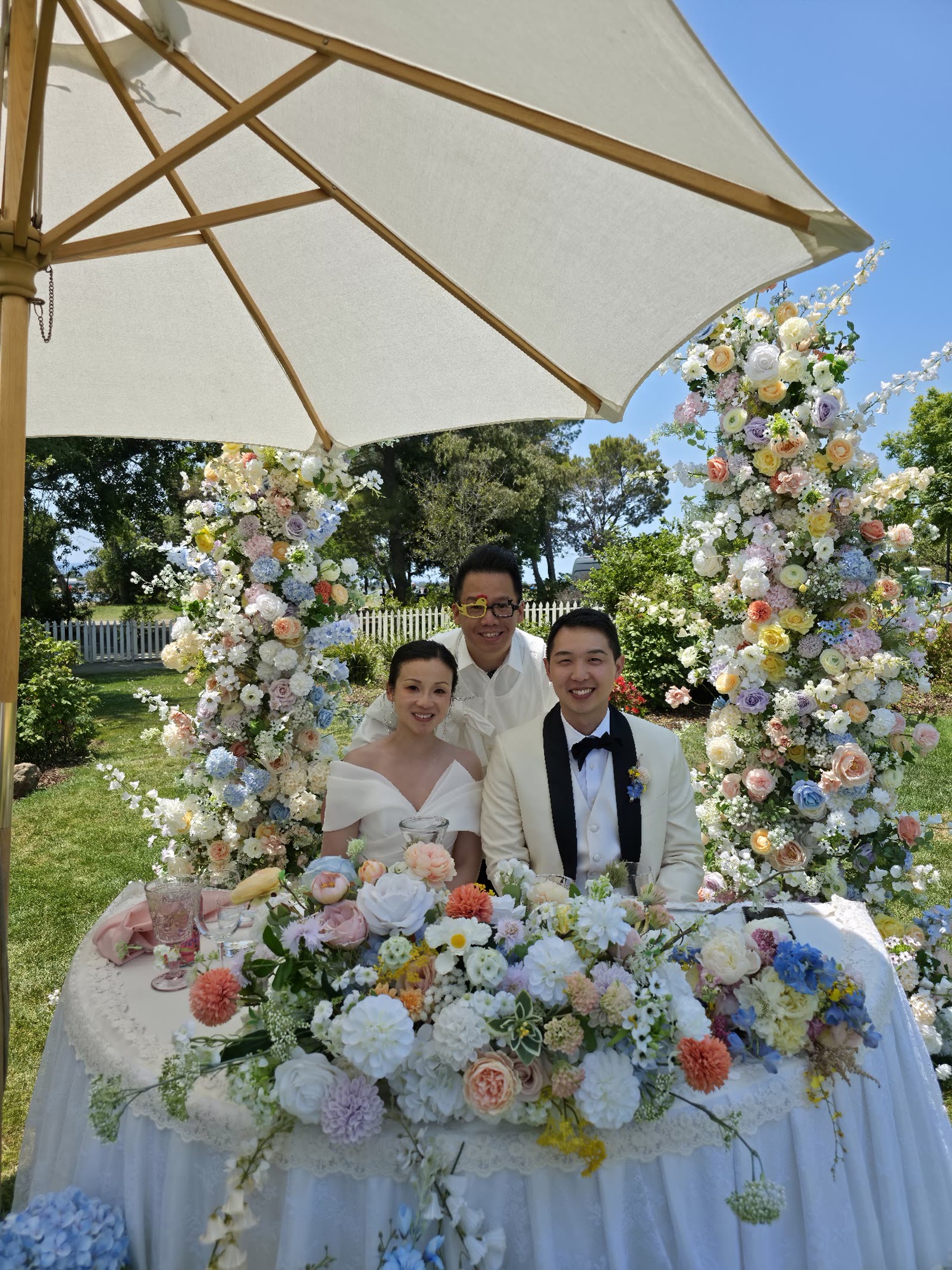 Foksifu with newlyweds at their sweetheart table under a floral arch at an outdoor Bay Area wedding